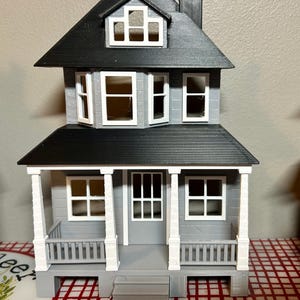 May include: A gray and black 3D printed model of a two-story house with a porch and white columns. The house has a black roof and white windows.