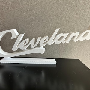 May include: White wooden sign with the word "Cleveland" in a cursive font.