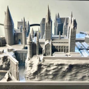 May include: A detailed 3D printed model of Hogwarts castle, a fictional school of witchcraft and wizardry from the Harry Potter series. The model is made of gray plastic and features intricate details, including towers, windows, and a surrounding landscape.