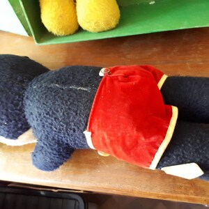 Puede incluir: Un juguete de peluche negro y amarillo con un traje de ba&ntilde;o de rayas rojas y blancas. El juguete est&aacute; acostado de lado con la cabeza apoyada en la superficie.