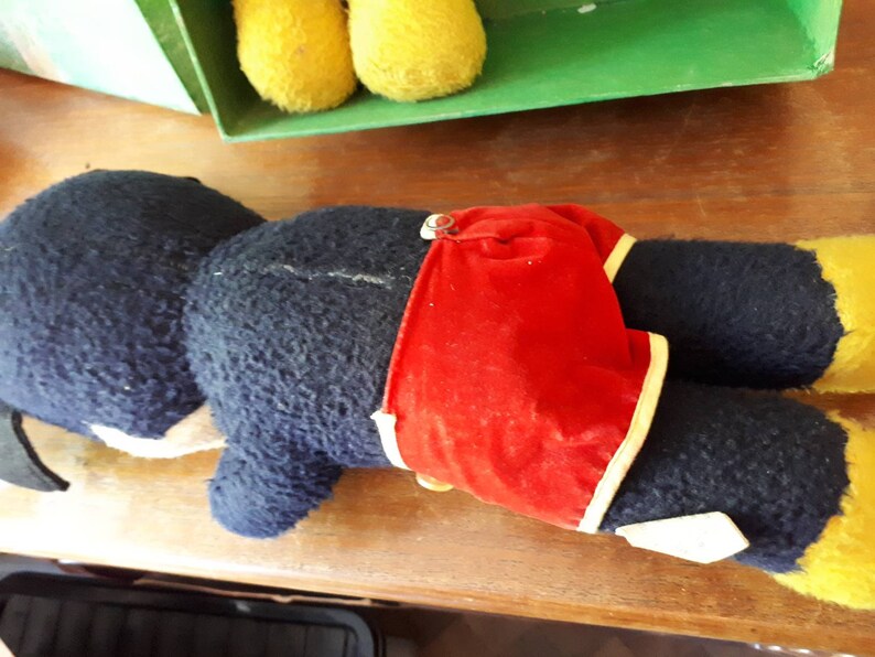 Puede incluir: Un juguete de peluche negro y amarillo con un traje de ba&ntilde;o de rayas rojas y blancas. El juguete est&aacute; acostado de lado con la cabeza apoyada en la superficie.
