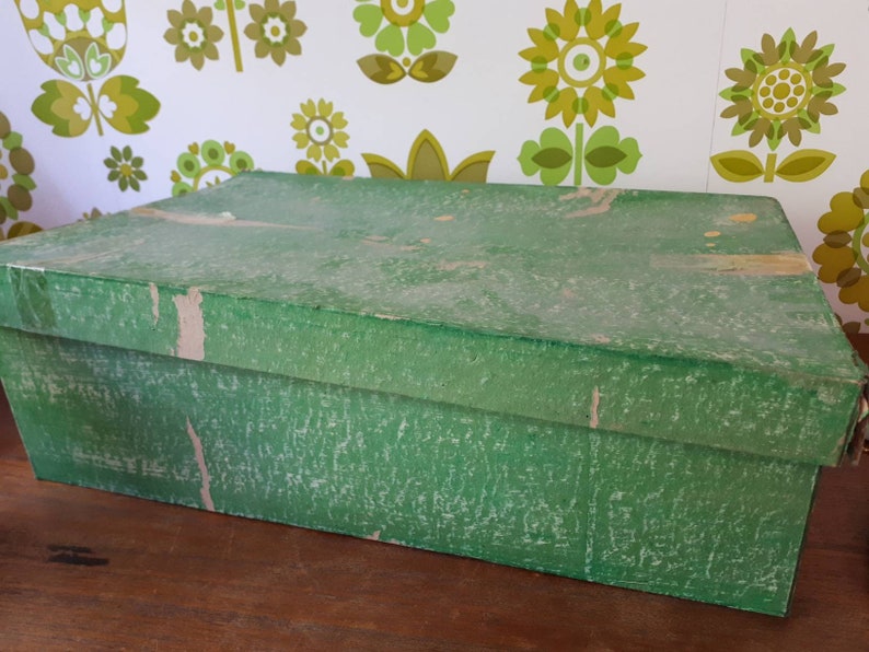 Puede incluir: Una caja de cart&oacute;n verde con una superficie texturizada. La caja est&aacute; cerrada y parece ser vintage.
