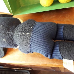Puede incluir: Un juguete de peluche negro y azul con una cola larga y una etiqueta blanca. El juguete est&aacute; acostado sobre una superficie de madera.