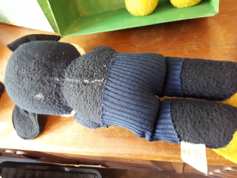 Puede incluir: Un juguete de peluche negro y azul con una cola larga y una etiqueta blanca. El juguete est&aacute; acostado sobre una superficie de madera.
