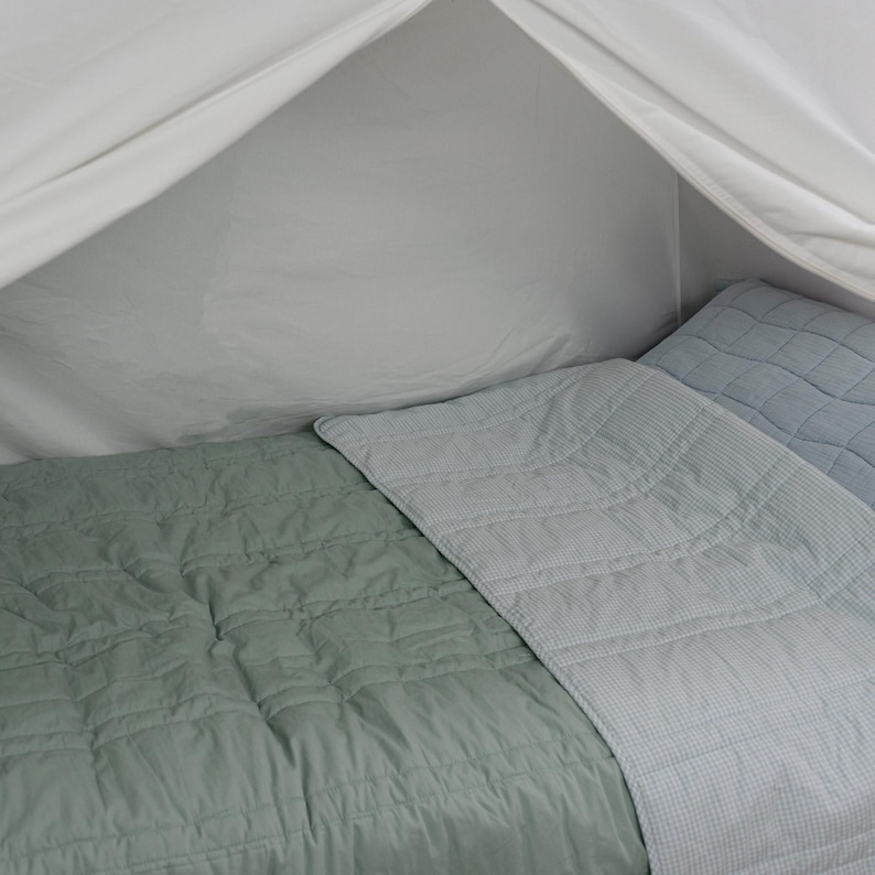 May include: A bed with a light green quilted blanket and a light blue quilted blanket. The bed is under a white canopy. The blankets have a diamond pattern.