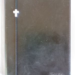 May include: A black leather-bound journal with a white cross and the text "Gold Fibre" embossed on the front cover.