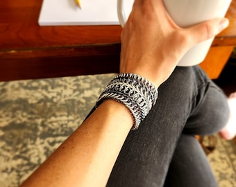 May include: A silver and black chainmail bracelet with multiple rows of interlocking metal rings.