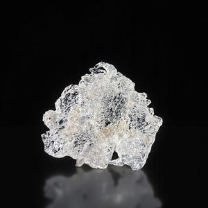 Può includere: Una scultura in vetro trasparente di forma irregolare con una superficie strutturata. L'opera d'arte è ambientata su uno sfondo nero, creando un contrasto che evidenzia i dettagli intricati e la forma del pezzo di vetro. Il riflesso della scultura è visibile sotto.