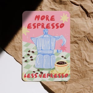 Könnte beinhalten: Rechteckiger Druck mit den Worten "MORE ESPRESSO LESS DEPRESSO". Das Bild zeigt eine blaue Kaffeemaschine, Kaffeebohnen und eine gelbe Kaffeetasse auf rosa und grünem Hintergrund.