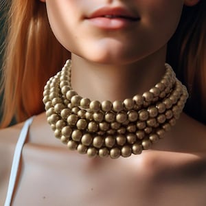 May include: A multi-strand beaded choker necklace in a gold tone. The necklace is made of large, round beads and is being worn by a person.