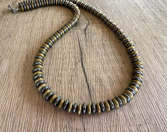 May include: A necklace featuring a repeating pattern of alternating metallic dark gray and matte gold-toned disc-shaped beads. The strand is arranged in a circular loop and includes a small silver-toned metal clasp at the end of the bead string.