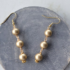 May include: Gold dangle earrings with four round gold beads on each earring.