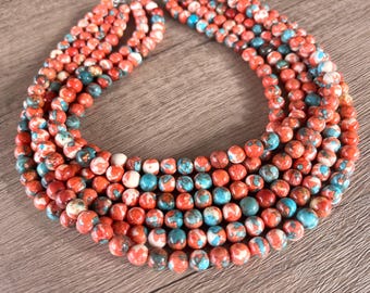 May include: A multi-strand necklace featuring round beads with a marbled pattern in shades of vibrant orange, bright turquoise, and white. The beads are arranged in several concentric rows, creating a dense, layered appearance with a polished finish.