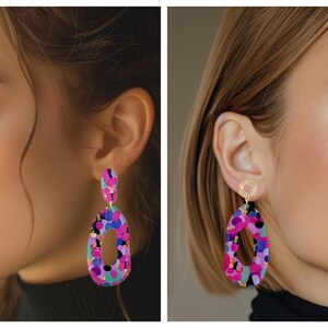Puede incluir: Un par de pendientes colgantes de forma ovalada con un patr&oacute;n abstracto colorido. Los pendientes est&aacute;n hechos de un material rosa, morado y azul con detalles dorados.
