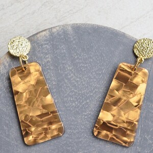 May include: A pair of gold and brown statement earrings with a geometric design. The earrings are made of a textured material and have a rectangular shape.