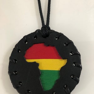 Pu&ograve; includere: Una collana in pelle nera con un ciondolo rotondo che presenta un'incisione del continente africano nei colori della bandiera panafricana: rosso, giallo e verde.