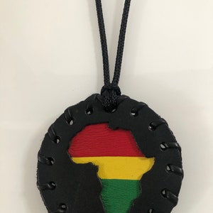 Pu&ograve; includere: Una collana in pelle nera con un ciondolo rotondo che presenta un ritaglio del continente africano nei colori della bandiera panafricana: rosso, giallo e verde.