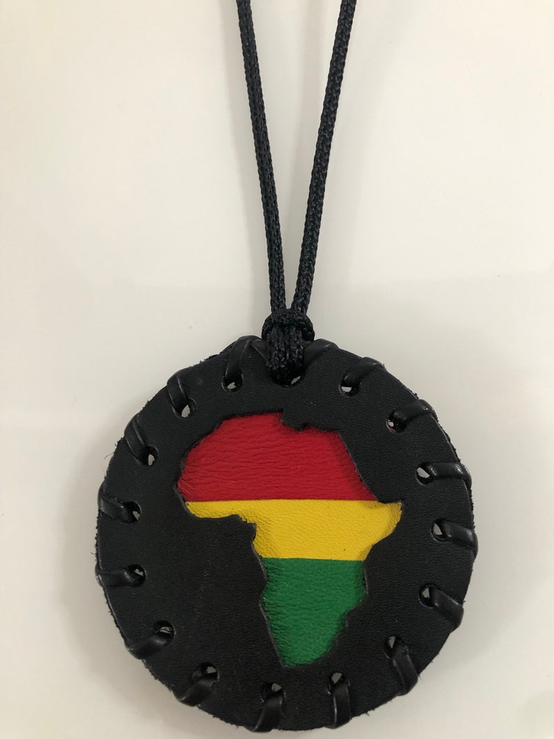 Pu&ograve; includere: Una collana in pelle nera con un ciondolo rotondo che presenta un ritaglio del continente africano nei colori della bandiera panafricana: rosso, giallo e verde.