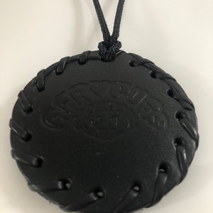 Pu&ograve; includere: Collana in pelle nera con un ciondolo rotondo che presenta la parola "Groovy" in un font stilizzato. Il ciondolo ha un bordo cucito e un cordino nero.