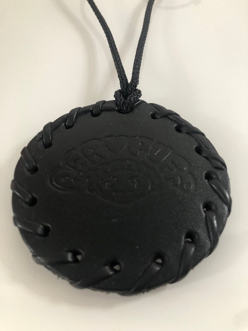 Pu&ograve; includere: Collana in pelle nera con un ciondolo rotondo che presenta la parola "Groovy" in un font stilizzato. Il ciondolo ha un bordo cucito e un cordino nero.