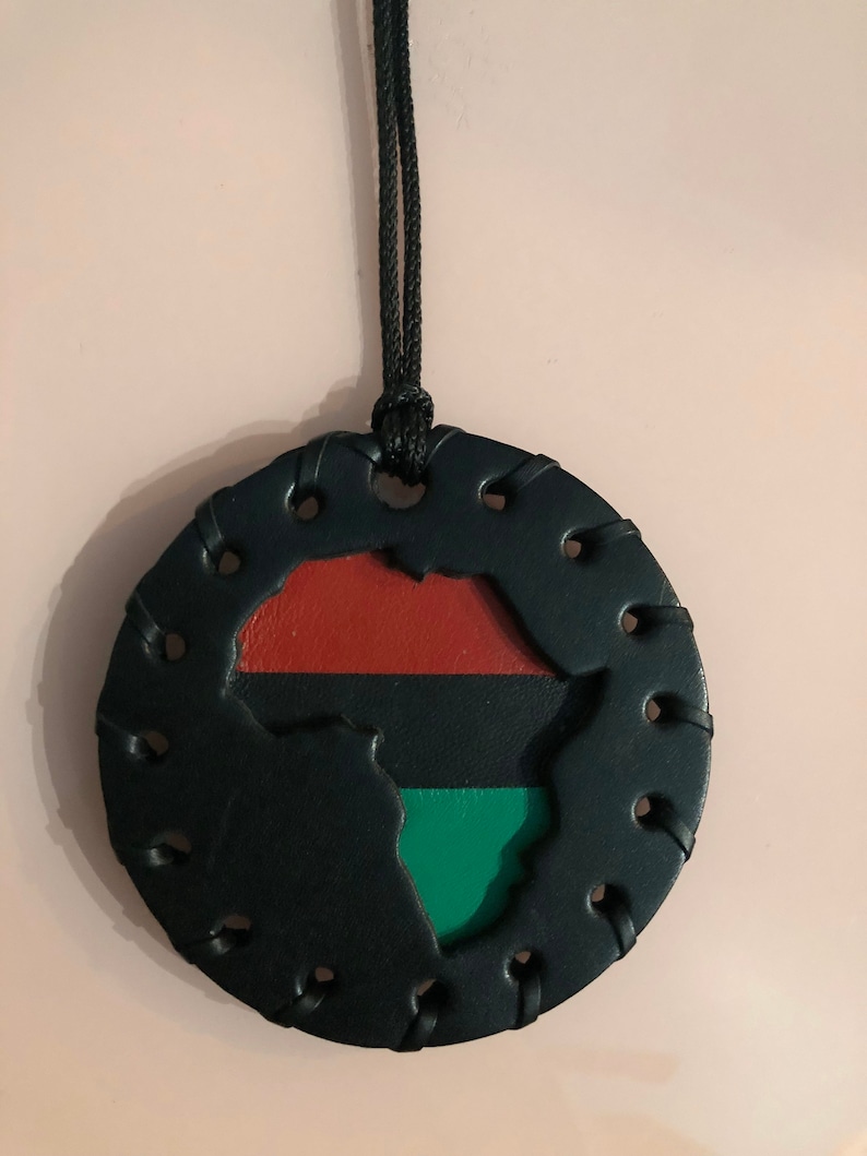 Pu&ograve; includere: Una collana in pelle nera con un ciondolo rotondo che presenta un ritaglio del continente africano. Il ciondolo &egrave; decorato con i colori della bandiera panafricana: rosso, nero e verde.