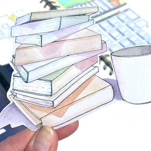 May include: A stack of colorful books with a white mug next to them. The books are stacked on top of each other and have different colored covers. The mug is white and has a handle.