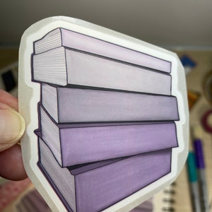 May include: A stack of five purple books with white pages. The books are stacked on top of each other and have a slightly faded look.
