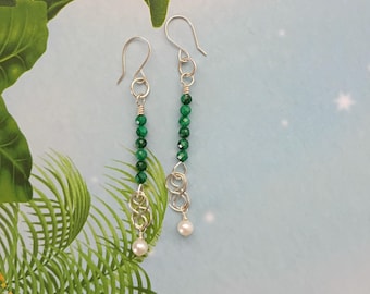 May include: A pair of long drop earrings featuring silver-toned ear wires, a vertical row of small faceted green beads, a silver-toned infinity-style metal link, and a single small white pearl bead at the bottom of each earring.
