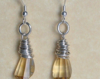 May include: A pair of dangle earrings featuring teardrop-shaped, faceted, amber-colored gemstones. The gemstones are wrapped with silver-colored wire and suspended from silver-colored ear wires.