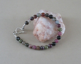 May include: A bracelet made with green, black, and pink gemstone beads. The bracelet has a silver clasp.