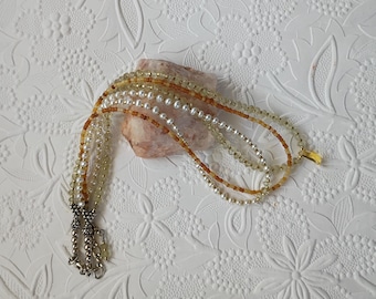 May include: A multi-strand necklace featuring white freshwater pearls, translucent light green beads, and amber-colored faceted beads. The strands are connected by silver-toned metal end caps and include a silver-toned metal chain extender.
