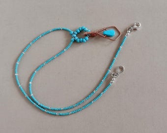May include: A turquoise beaded necklace with a copper wire pendant featuring a turquoise stone. The necklace has a double strand design and silver-colored clasps. The beads are small and evenly spaced.