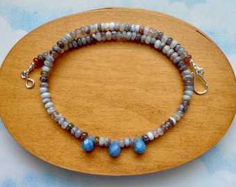May include: A silver necklace with a double strand of gray agate beads and three blue teardrop-shaped stones hanging from the bottom.