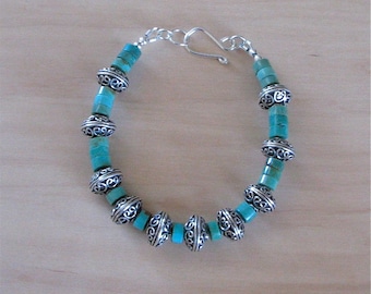 May include: A turquoise and silver bracelet with a silver clasp. The bracelet is made of round turquoise beads with silver accents.