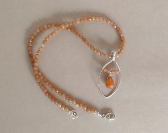 May include: A necklace featuring a strand of small, faceted, light orange beads. A silver-toned wire pendant in a marquise shape hangs from the strand, enclosing a single, larger, teardrop-shaped orange bead suspended in the center.