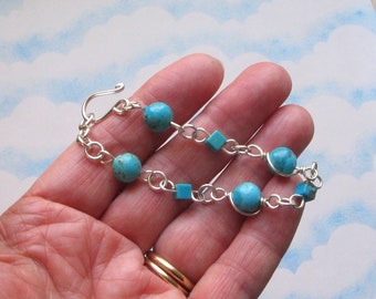 May include: A silver chain bracelet with turquoise beads and square accents. The bracelet has a hook clasp.
