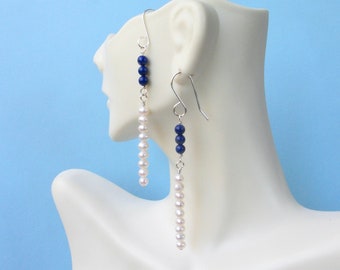 May include: A pair of dangle earrings with white pearls and blue lapis lazuli beads. The earrings are silver and have a hook closure.