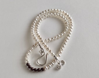 May include: A white pearl necklace with a small strand of dark purple beads at the bottom. The necklace has a silver clasp.
