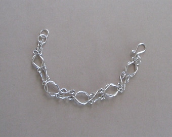 May include: A silver bracelet with a delicate, intricate design. The bracelet is made of multiple linked loops, creating a flowing, organic pattern.