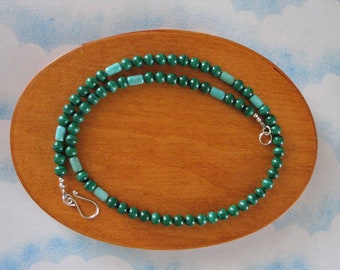 May include: A green malachite bead necklace with silver clasp. The necklace is on a wooden surface.