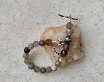May include: A gray agate beaded bracelet with a silver toggle clasp. The beads are faceted and have a natural, earthy look.