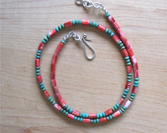 May include: A necklace made with red coral and turquoise beads. The necklace is strung on a silver chain with a lobster clasp.