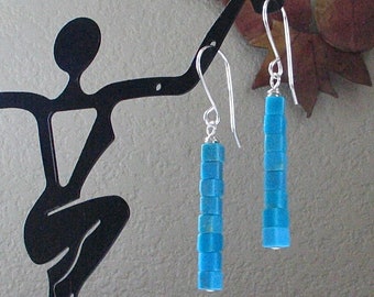May include: A pair of dangle earrings with a silver hook and a turquoise blue bead drop. The beads are stacked in a column and are square shaped.