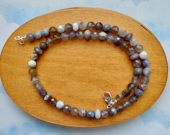 May include: A necklace made of faceted gemstone beads in shades of gray, brown, and white. The beads are strung on a silver chain with a silver clasp.