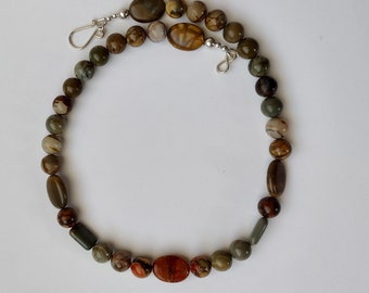 May include: A brown and green stone necklace with a silver clasp. The necklace is made of round and oval-shaped stones.
