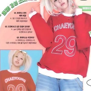 May include: A red sweatshirt with the name "CHAEYOUNG" and the number "29" in white. The person in the image is wearing light blue jeans and sunglasses. The image also contains Korean text.