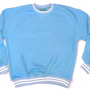 May include: A light blue sweatshirt with long sleeves and a crew neck. The cuffs and hem feature white and light blue stripes. The neckline has a white and light blue striped trim. The garment is made of a soft material.