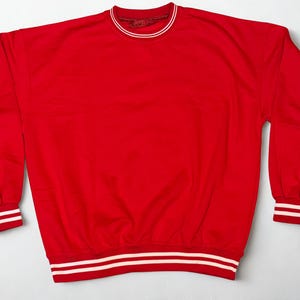 May include: A bright red sweatshirt with a crew neck and long sleeves. The collar, cuffs, and hem feature white stripes. The sweatshirt is made of a soft material and is suitable for casual wear.