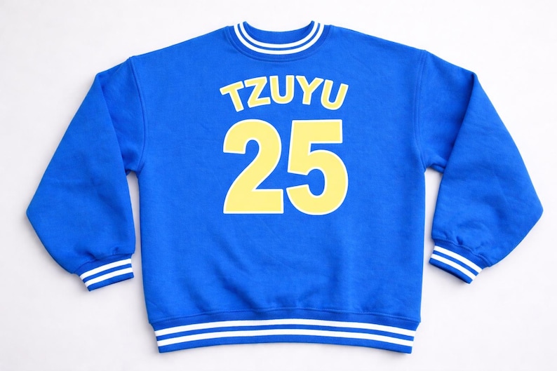 May include: A royal blue sweatshirt with the name "TZUYU" in yellow block letters above the number "25". The sweatshirt has white and yellow striped details on the collar, cuffs, and hem.