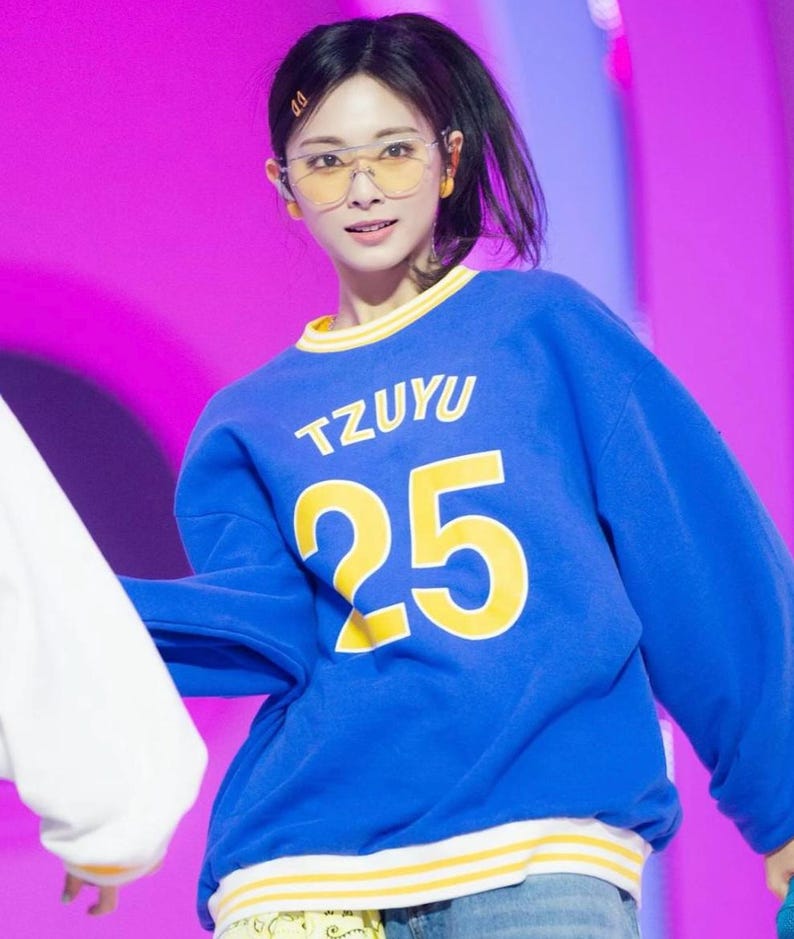 May include: A person wearing a blue sweatshirt with the word "TZUYU" and the number "25" in yellow. The sweatshirt has yellow and white trim. The person is also wearing yellow-tinted glasses.